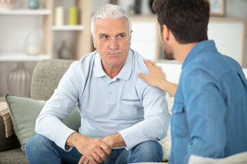 son comfort his aged father sitting on couch