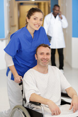 happy female doctor carrying male patient on wheelchair