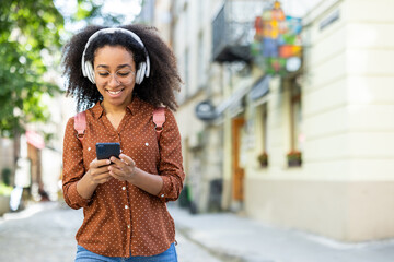 Young woman enjoying music on headphones while using phone outdoors