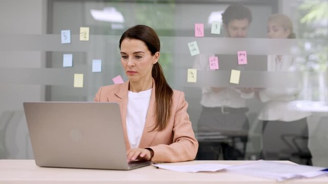 Stylish businesswoman, a director or marketing manager, works efficiently at her laptop in a modern coworking office. Ideal for themes of professionalism and workspace productivity.