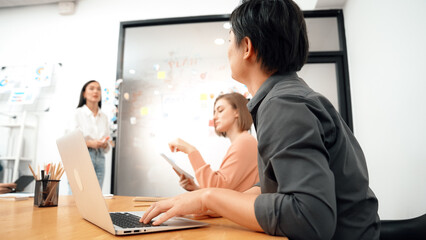 Young beautiful investor shares marketing strategy with attentive businesswoman in front of a glass board with colorful sticky notes and mind maps at creative business meeting room. Immaculate.