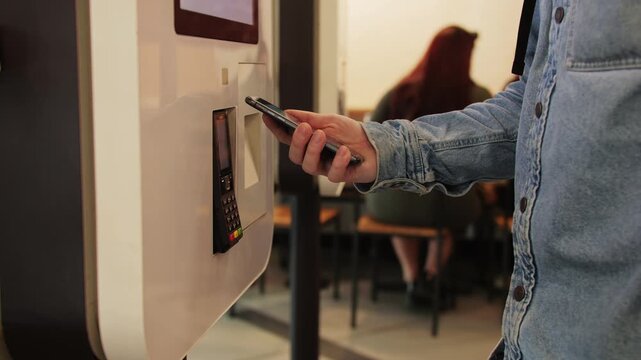 A man is using his smartphone for digital payment at a selfservice kiosk in a cafe, fast food purchase, restaurant. 