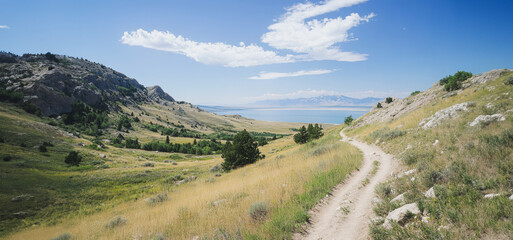 Fototapeta premium Scenic Hiking Trail Along Rolling Hills and Calming Waters Under a Clear Blue Sky