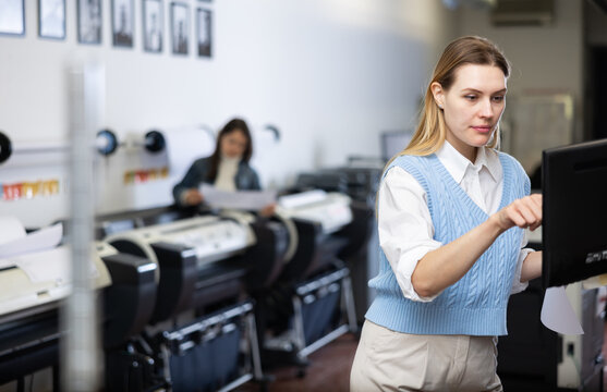 Woman using printer while working in print shop. Female printshop worker using printing device, pushing buttons.