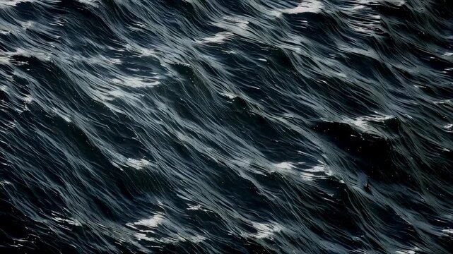 A close-up view of dark ocean waves reflecting light at night. The water appears textured and shimmering, creating a moody, dramatic effect. The scene exudes tranquility and power.