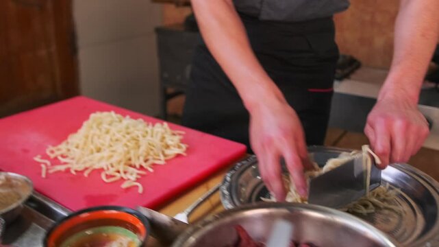 Sliced ​​white noodles for lagman are placed on a plate by the hands of a cook using a large knife among different spices for preparing oriental dishes, close-up.