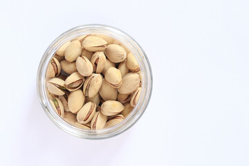 Pistachios in a glass jar on a white background. A handful of dry salted pistachios on a light background, selective focus. Pistachio with shell. Close-up