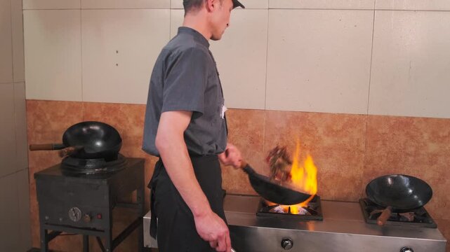 Male chef with ladle adds various spices paprika salt sesame glutamate cumin to the meat being prepared for pilaf in an Uzbek dish.