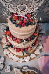 Three-tier wedding cake topped with fresh berries and surrounded by cookies.