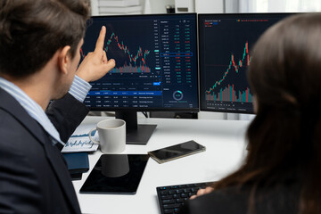 Two business traders discussing on dynamic stock market in currency rate investment trading on two pc screens with compare real time graph on risk or profit point of data at modern office. Postulate.