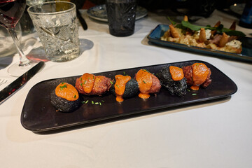 Black and brown cod fritters with romesco sauce on a black tray on a white tablecloth on a restaurant table or at home
