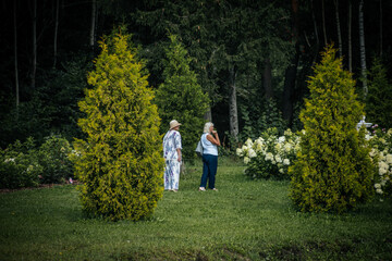 Fototapeta premium The women admire the colorful garden filled with a variety of flowers, including red, purple and yellow flowers, against a backdrop of greenery and white hydrangeas.