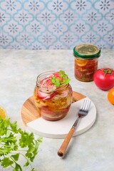 Salad sliced ​​fast pickled tomatoes with onions in a glass jar on a gray concrete background. Harvesting, conservation, pickled vegetables.