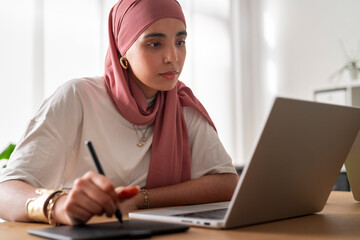 A woman in a dark red hijab works intently on her laptop, likely programming or designing for a 3D printing project. 