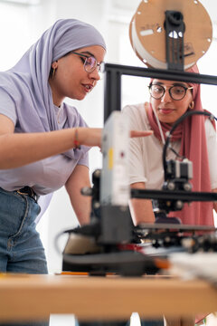 Two women in hijabs collaborate on setting up a 3D printer, carefully adjusting and calibrating the machine. Their teamwork emphasizes precision and technical skills in engineering.