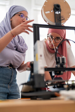 Two women in hijabs collaborate on setting up a 3D printer, carefully adjusting and calibrating the machine. Their teamwork emphasizes precision and technical skills in engineering.