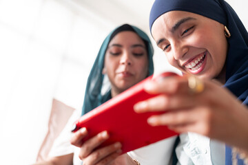 A woman in a dark blue hijab is deeply focused on playing a game on a tablet. Her concentration highlights the immersive nature of modern digital entertainment.