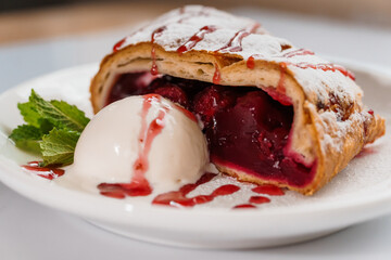 Dessert strudel with cherry and ice cream on a white plate