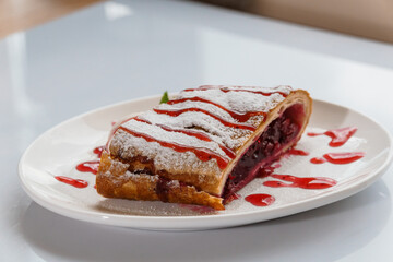 Dessert strudel with cherry and ice cream on a white plate