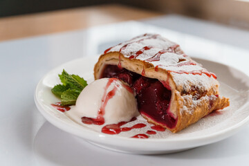 Dessert strudel with cherry and ice cream on a white plate