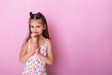 Happy little girl eating ice cream in a cone on a pink background. So yummy. Closeup photo of beautiful funny little lady. A child holds ice cream in his hand in a cup on a pink background.