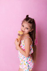 Happy little girl eating ice cream in a cone on a pink background. So yummy. Closeup photo of beautiful funny little lady. A child holds ice cream in his hand in a cup on a pink background.