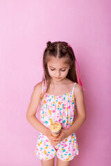 Happy little girl eating ice cream in a cone on a pink background. So yummy. Closeup photo of beautiful funny little lady. A child holds ice cream in his hand in a cup on a pink background.