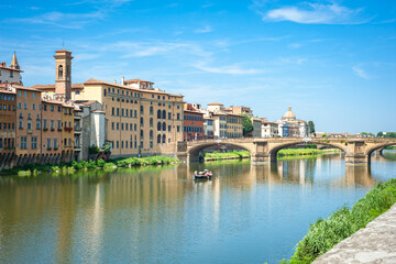 Rowing boat in the Arno River with historic buildings and the Santa Trinita Bridge in in Florence, Italy