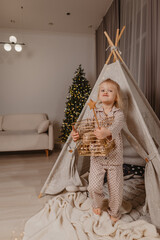 An attractive blonde girl in pajamas  is having fun in a wigwam on the background of a Christmas tree  © Татьяна Добрикова