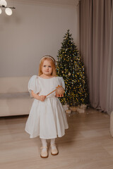 A beautiful blonde girl in a white dress waves a magic wand on the background of a Christmas tree