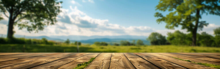 A horizontal image showing a wooden surface with visible textures and green leaves in the top left corner, against a blurred natural landscape background. Suitable for use as a serene, nature-themed b