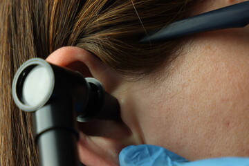 Close up view of a woman’s ear and a otoscope inside it examine by a professional wearing gloves 