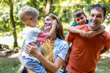 Family of four bonding in the park. Mother and father hugging with their sons.
