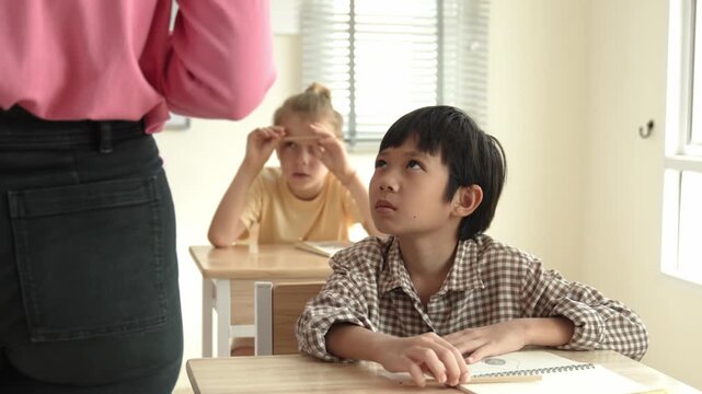 Asian elementary student looking at teacher while attend in classroom. Diverse smart student sitting at classroom while listening teacher explain about classwork or test. Education concept. Pedagogy.
