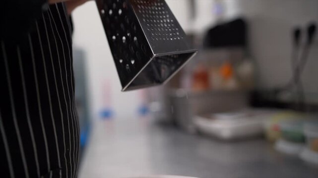 queso rayadoA close-up shot of a chef expertly grating cheese with a handheld grater. The chef's hands are steady as they work, creating fine, delicate shreds of cheese that fall onto a clean surface 