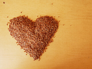 Pile of uncooked buckwheat in a heart shape on a wooden table surface. Popular Russian porridge and meal. Healthy grain. Organic product.