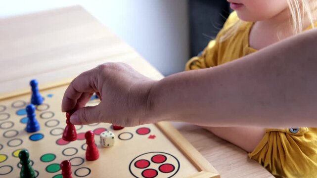close-up of hands of small child manipulate with wooden figurines of family board game, smart kid, 2-year-old girl is learning to count, Cross and circle game Parcheesi, foreground focus