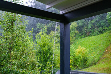 Fototapeta premium Streams of rainwater pour down the roof gutters onto a porch.
