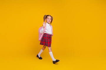 Full body portrait of little schoolkid walk hand wave hi wear uniform isolated on yellow color background