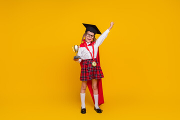 Full body photo of small schoolchild uniform mortarboard cup medal raise fist isolated on yellow color background