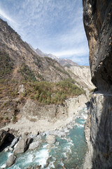 Experience the stunning beauty of a nepalese river winding through majestic mountains and lush greenery under a serene blue sky, inspiring awe and wanderlust