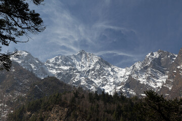 Majestic snow-capped mountains tower over lush green forest in the himalayas on a sunny day, creating a stunning view perfect for outdoor adventures like trekking and hiking