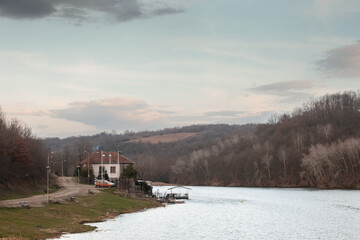 Panorama of a European natural lake, on Duboki Potok jezero lake, by Barajevo, in the southern rural part of Belgrade, Serbia, during a cloudy winter afternoon, surrounded by a grey forest.