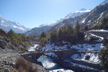 Fast flowing, glacial river cuts through the snow covered himalayas mountain range, a wooden bridge...