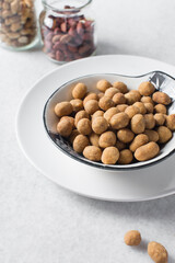 Fried coated peanuts in a white ceramic plate, cracker peanuts on a marble countertop, nigerian peanut snack in a small white plate