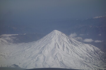 Snow covered volcanic peak is standing tall above a vast mountainous landscape, showcasing the raw beauty and power of nature