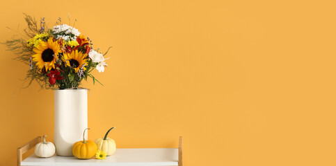 Shelving unit with bouquet of autumn flowers and pumpkins near orange wall