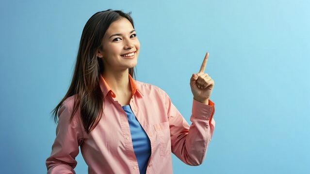 Mujer modelo posando se&ntilde;alando con el dedo &iacute;ndice hacia arriba, fondo azul, rostro expresivo. 