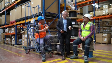 Group of male workers, blue collar worker and business manager man taking coffee break eating breakfast holding coffee mugs and talking during the shift break in a factory warehouse. - Powered by Adobe