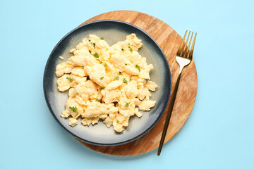 Plate of scrambled eggs with herbs on light blue background